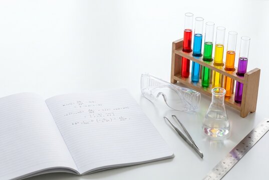 Open lab notebook with rack of vivid colored test tubes safety goggles on white desk, STEM education science