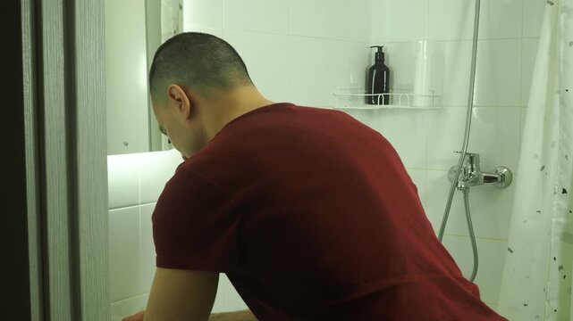 Morning routine. A man washes his face in front of a mirror.
