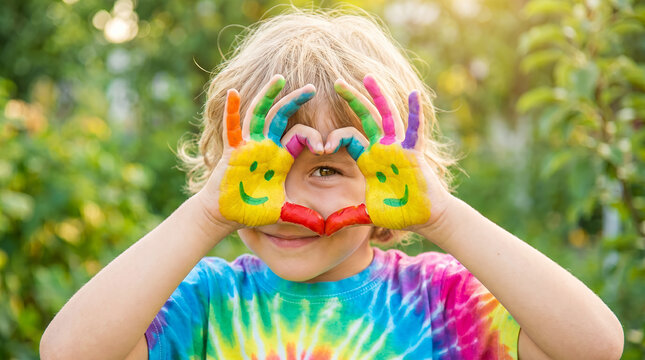 Happy child showing colorful hands and making a heart shape in a garden