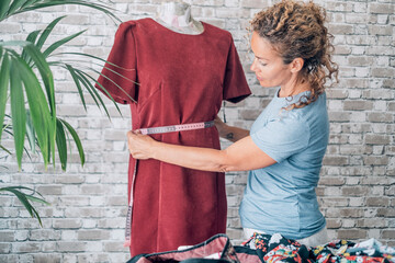 Obraz premium Professional woman fashion designer working in her creative studio, taking measurements of a new red dress on a mannequin while creating a custom design