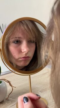 Teenage girl with acne problem skin checking her reflection in the mirror, feeling sad about imperfections and showing lack of self-confidence and insecurity