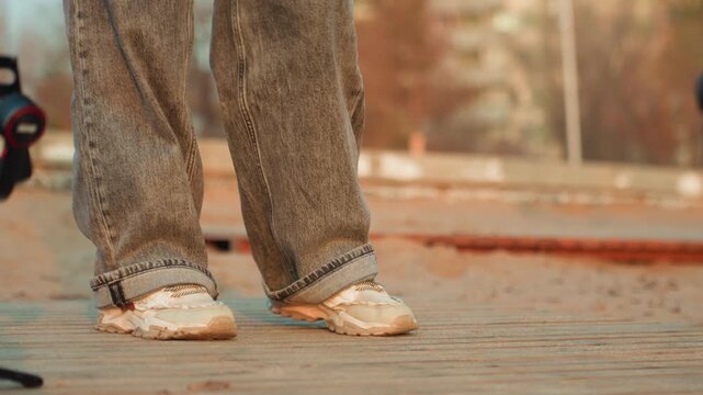 Closeup sneakers walking on pavement, autumn evening scene with baggy frayed jeans, scooter wheel peek, warm muted tones, textured concrete, steady footsteps, solitary wander, nostalgic urban mood