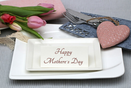 Festive table decoration for Mother's Day: plate, cutlery, napkin, flowers and a heart with the inscription "Happy Mother's Day" on a card.