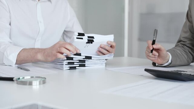 Professionals handling a large stack of documents and paperwork, signing a contract in a busy office. Audit and taxes in business