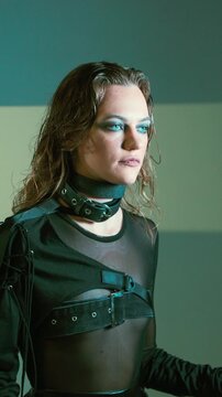 Medium shot portrait of young blue-eyed woman with long hair, bold makeup and leather harness