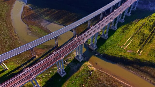 Elevated perspective of two parallel concrete bridges, one for cars and one for trains, supported by high pillars over a river. High angle view of road and railway viaducts.