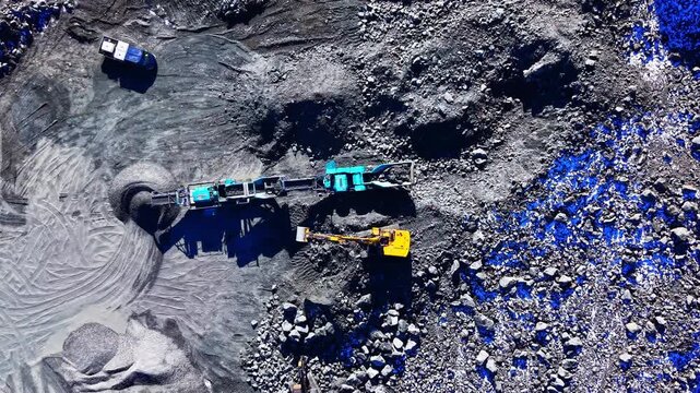 Mobile stone crushing equipment and yellow excavators processing rocks in a quarry environment. Industrial stone crushing plant and excavators at mining site.