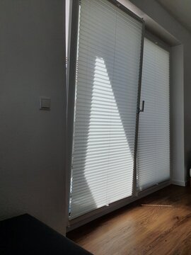 Modern White Plisse Blinds on Tilt and Turn Window in Minimalist Interior. Interior shot of a modern room featuring white pleated blinds (plisse) on a large tilt-and-turn window. 