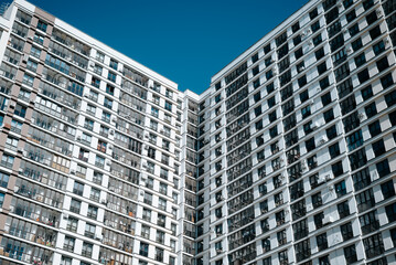 Fototapeta premium Two tall apartment buildings stand side by side under a clear blue sky. Their glass and concrete facades reflect the sunlight, showcasing urban living in a vibrant environment