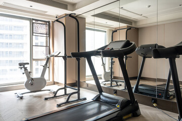 Naklejka premium Modern fitness gym interior featuring treadmills, stationary bikes, and exercise equipment with mirrored walls and natural light