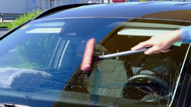 Man cleaning car windshield with squeegee at gas station after refueling, improving visibility and road safety, vehicle care and maintenance concept.