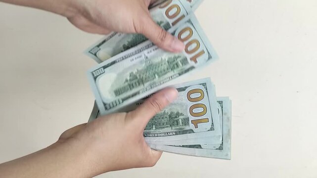 Close-up of two hands holding and counting US 100 Dollar bills against a clean white background. Realistic image showing money handling, finance, wealth, and cash payment concept