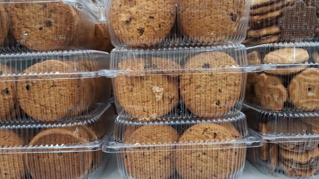 Rows of oatmeal cookies in transparent plastic containers on a supermarket shelf. Mass-produced baked goods for retail sale. Concept of grocery shopping, snack variety, and food industry packaging