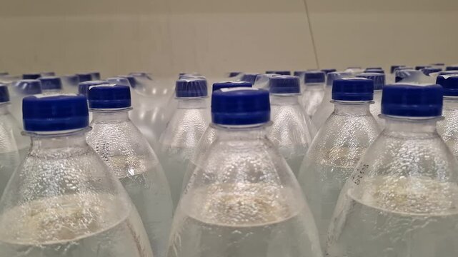 Close-up of multiple plastic water bottles with blue caps in transparent shrink wrap. Rows of bottled mineral water in warehouse or supermarket shelf. Group of clear PET bottles. Healthy lifestyle