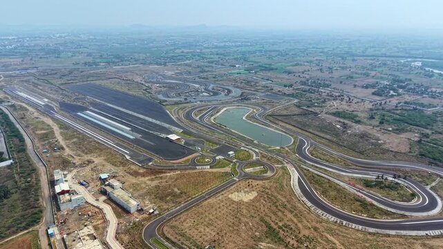 Drone shot of a tyre testing facility featuring winding test tracks with sharp curves and loops. Surrounded by open land and industrial buildings, the track shows controlled conditions used for vehicl