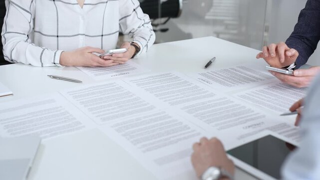Business people collaborating on contracts and agreements during an important boardroom meeting, navigating legal documents and using mobile phones for quick communication and data access