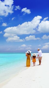 A elegant family in summer dresses walks on a tropical paradise beach with turquoise ocean and white sand during their vacation time