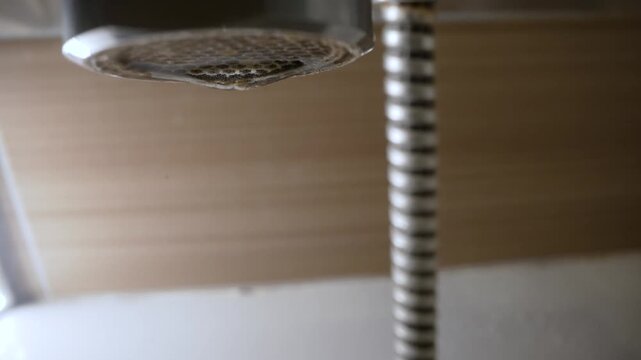 Macro shot of a single water drop forming on a leaky faucet aerator. Close up detail of a dripping tap, symbolizing water waste, conservation, and scarcity. Neutral background