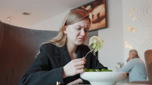 Caucasian woman at bistro pondering salad quality, professional jacket and pensive expression, white bowl of greens, hesitant bite and thoughtful posture, warm ambient lights and distant diner
