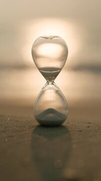 Glass hourglass on a sandy shore glowing in golden sunlight, representing time, waiting, deadlines, change, reflection, and the precious balance between past, present, and future.