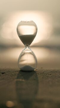 Glass hourglass on a sandy shore glowing in golden sunlight, representing time, waiting, deadlines, change, reflection, and the precious balance between past, present, and future.