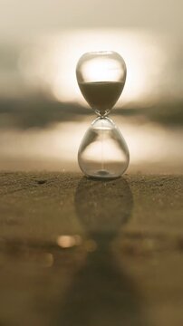 Glass hourglass on a sandy shore glowing in golden sunlight, representing time, waiting, deadlines, change, reflection, and the precious balance between past, present, and future.