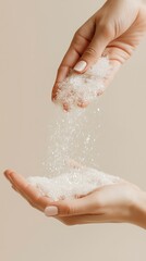 Fototapeta premium Woman hands pouring sparkling white granulated sugar from upper hand to lower hand against soft plain beige minimalist neutral background