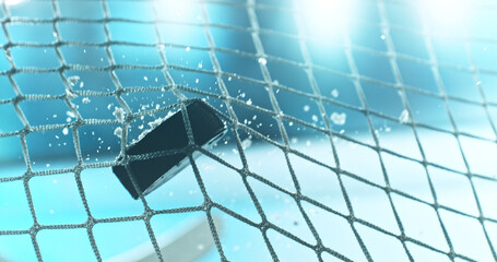 Action sports photo of a hockey puck flying into the goal net during a scoring shot, with ice particles in the air and a hockey stick visible in the background, capturing speed and intensity. © Jag_cz