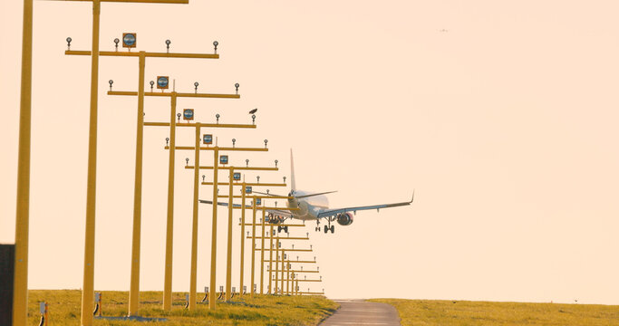 Passenger airplane approaching runway aligned with airport approach lighting system during golden hour. Perspective view of aviation infrastructure.