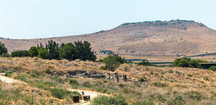 Horizontal high angle wide shot of the arid mountainous border landscape between Israel and Jordan, featuring valley views, roads, olive tree orchards, and rural settlements in bright daylight