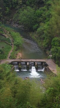 Mountain stream flowing over a concrete weir dam with cascading water and lush green surroundings