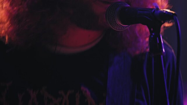 Dynamic close-up of a rock musician with long red hair headbanging into a microphone. Energetic live performance at a concert with moody purple and red stage lighting creating an intense atmosphere