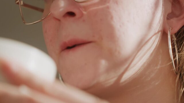 Closeup woman testing face cream for acne prone skin, wearing glasses, sampling from jar, contemplative expression, soft morning light, intimate skincare moment showing visible pores and texture