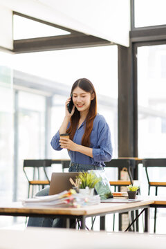 Young asian woman talking on smartphone holding coffee
