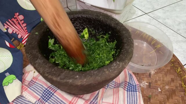 Hands are pounding pounding cassava leaves and pumpkin pieces use mortar and pestle made of stone. 