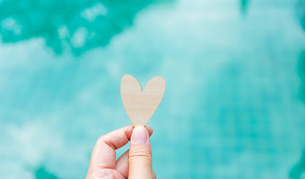 Wooden heart in girl hand over blurred blue water background, love and romance concept, valentine background idea