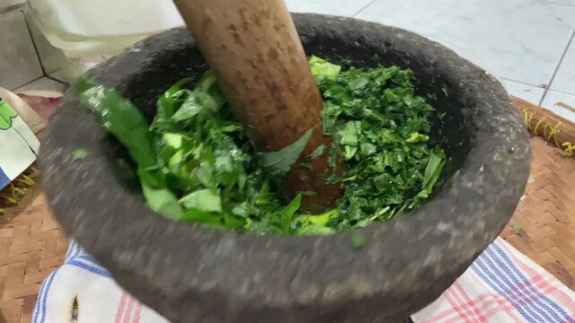 Hands are pounding pounding cassava leaves and pumpkin pieces use mortar and pestle made of stone. 