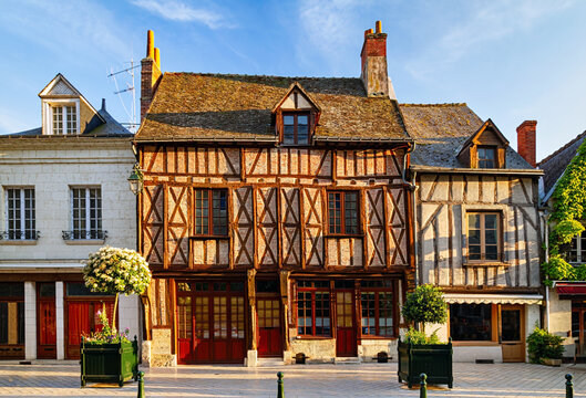 Sunlit historic half timbered houses with wooden beams, red doors, flower planters, and charming old town architecture under a blue sky, Amboise, France.