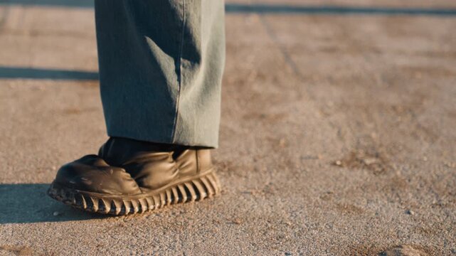 Walking carefully across frosty pavement. Closeup of footwear leaving textured imprints on frozen ground during sunset. Detailed shot of boots traversing icy surface while on rooftop at golden hour