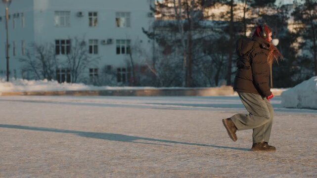 Female person maintaining stability outdoors in cold. Woman with red gloves improving equilibrium on icy surface. Female individual wearing warm clothing finds her footing on frozen parking lot