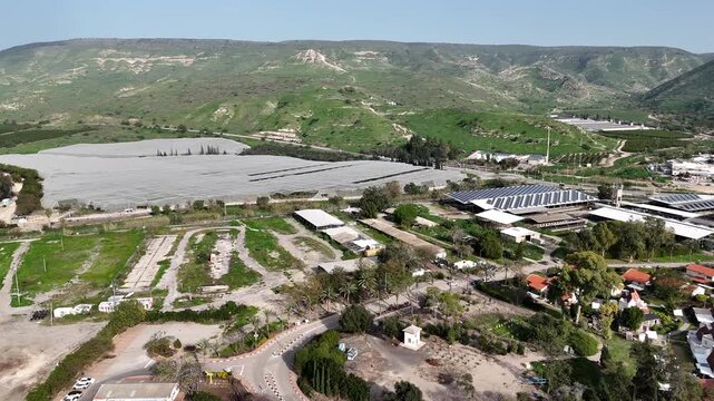Aerial view of Ein Gev kibbutz and agricultural fields with Golan Heights backdrop fly into Sea of Galilee sunset view