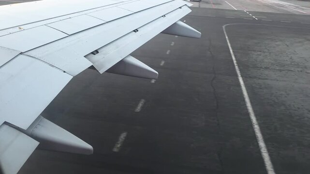 Airplane wing and aircraft parts visible from passenger window, taxiing on asphalt runway preparing for takeoff or landing at the international airport, symbolizing travel and aviation