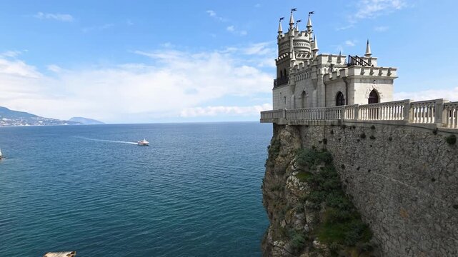 Swallow's nest castle, a neo-gothic architectural landmark, perching on a dramatic cliff face overlooking the tranquil blue waters of the black sea, with a distant boat navigating the water