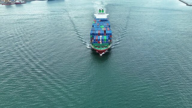 container ship fully loaded with colorful cargo containers being assisted by tugboats in the open sea. Concept of global maritime logistics, international trade, and heavy shipping operations.	