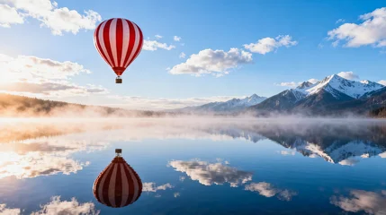 Fototapete Reflection A red striped hot air balloon drifts over a glassy alpine lake at sunrise, with snow-capped mountains, misty shoreline and fluffy clouds reflected in the still water.  © jianhua