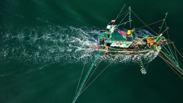 Cinematic bird's-eye view of an authentic wooden fishing boat navigating calm ocean waters in Southeast Asia.