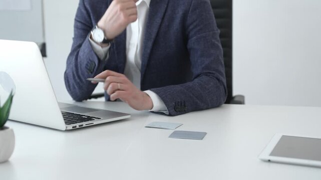 Professional businessman in glasses working on a laptop, analyzing financial data and charts in a modern, bright office setting, focusing on business growth and strategy