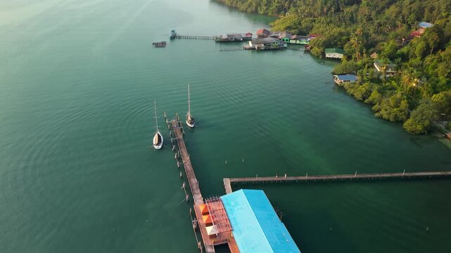 Aerial view of traditional stilt houses and a long wooden pier in a tranquil tropical bay.