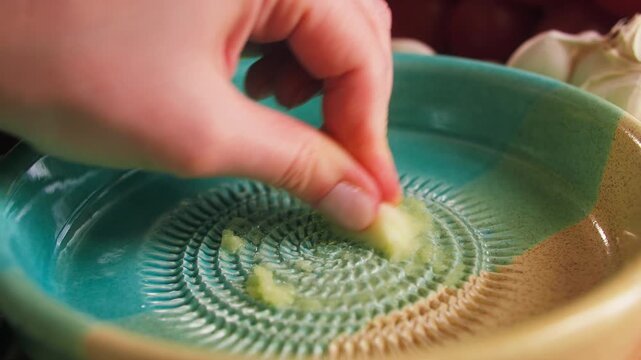 Hand grating fresh garlic on ceramic garlic grater plate, traditional Spanish ajo rallador. High quality 4k footage