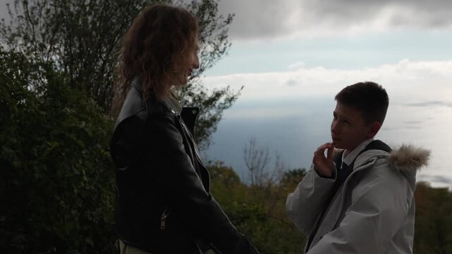 Mother son talking family bonding moment outdoors overlooking the sea on a cloudy day.